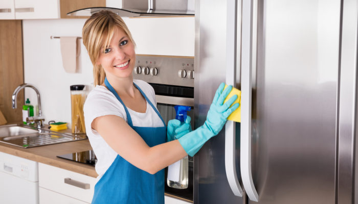 Woman cleaning refrigerator Young Smiling Professional Cleaning Service Woman Cleaning Refrigerator In Kitchen